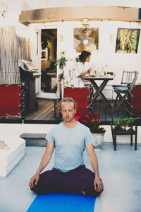 Man doing yoga while businesswoman sitting behind using laptop at houseboat