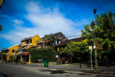 Street by trees and buildings against blue sky