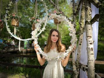 Portrait of smiling young woman standing against trees