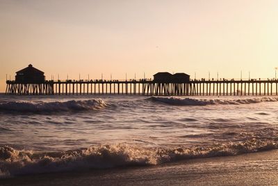 Pier on beach against clear sky during sunset