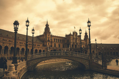 Bridge over river in city against cloudy sky