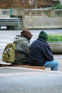 Rear view of people with hooded shirts sitting on retaining wall