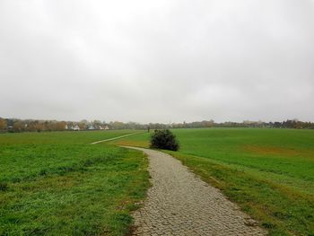 Dirt road amidst field against sky