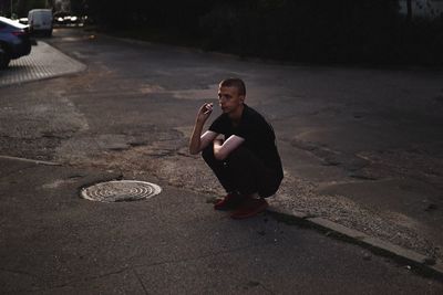 Man smoking cigarette while crouching on city street