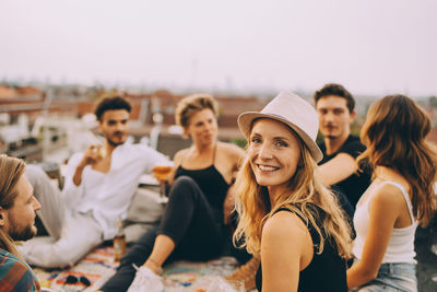 Portrait of smiling woman sitting with friends at terrace during rooftop party