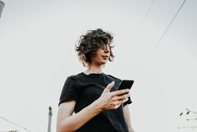 Young woman using mobile phone against clear sky