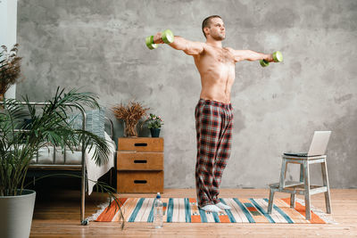 The athlete in home pajamas does morning exercises with dumbells, bends and pulls 