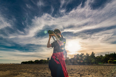 Woman standing on field against sky during sunset