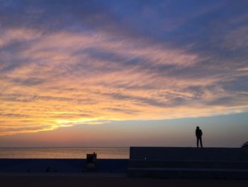 Silhouette man standing at beach against sky during sunset