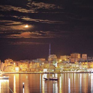 Illuminated buildings by river against sky at night