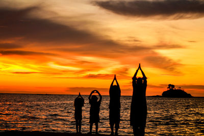 Silhouette people at sea against sky during sunset