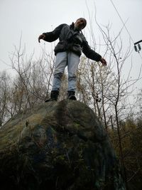 Low angle view of man standing on rock against sky