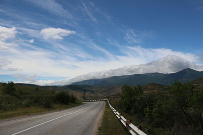 Empty road leading towards mountains against sky