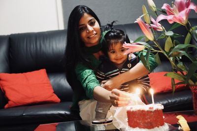 Portrait of smiling mother igniting candles on cake with son at home