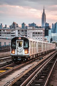 Train on railroad tracks by buildings in city against sky