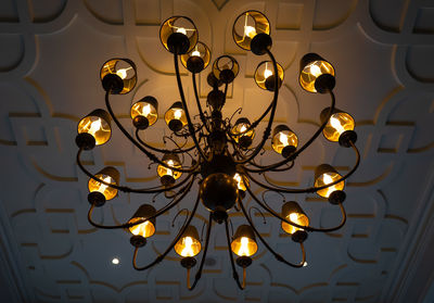 Low angle view of illuminated chandelier hanging from ornate ceiling