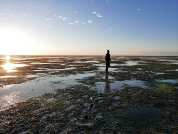 Silhouette man standing on wet landscape against sky at beach during sunset
