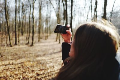 Woman photographing through smart phone in forest