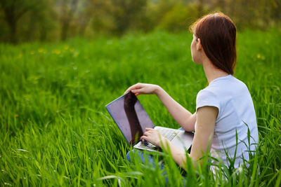 Young woman using laptop while sitting on field