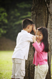 Portrait of girl playing hide and seek with brother at park