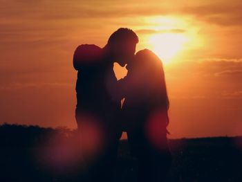 Silhouette couple kissing against sky during sunset