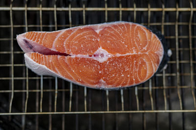 Close up of fresh salmon steak prepared for grilling with grains of salt on it, lies on grill mesh