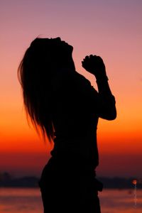 Silhouette of woman against orange sunset sky