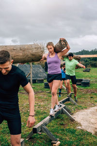 Men and women walking with logs on metal against sky