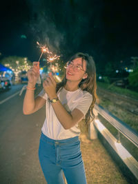 Young woman smiling while standing against sky at night