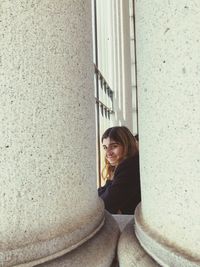 Portrait of smiling young woman sitting against wall