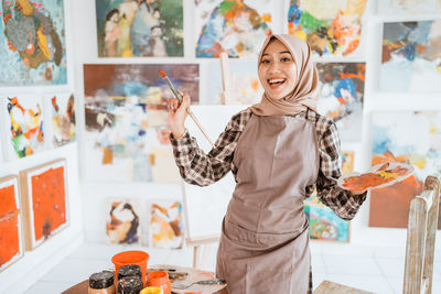 Portrait of smiling young woman with arms raised standing in restaurant