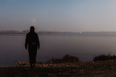 Rear view of man standing at lakeshore against sky