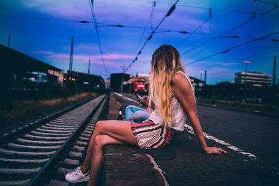 Woman sitting on railroad track against sky
