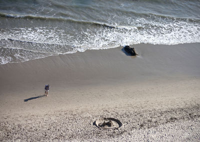 High angle view of man walking on shore with sandcastle at beach