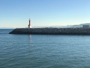 Lighthouse by sea against clear sky