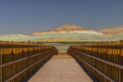 Footbridge leading towards mountains against clear sky