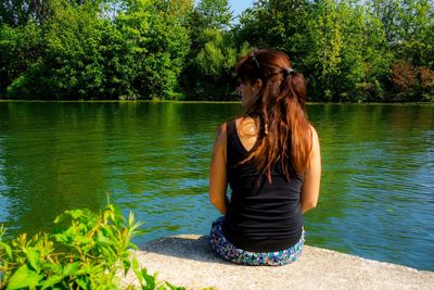Full length of woman sitting by lake against trees
