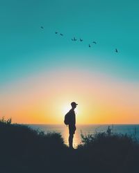 Silhouette man flying over sea against sky during sunset
