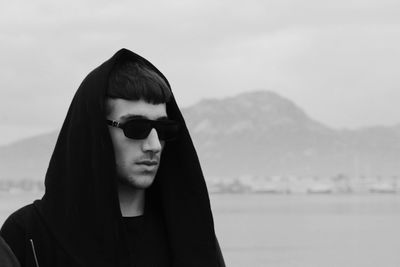 Boy in sunglasses and hooded shirt against sky