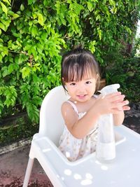 Portrait of girl with spray bottle on high chair at yard