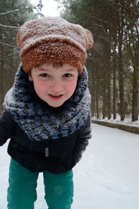 Close-up portrait of happy boy standing on snow covered field against trees