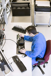 High angle view of mature male electrician working on machine part at desk in industry