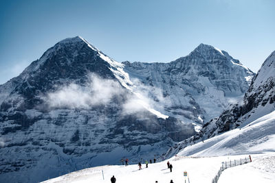 People by snowcapped mountains against clear sky