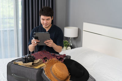 Young woman using mobile phone while sitting on bed at home