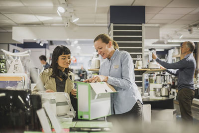 Mature female owner showing appliance to young customer in electronics store