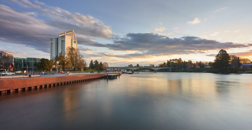 Scenic view of river by buildings against sky during sunset