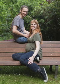 Portrait of pregnant woman with man sitting on bench