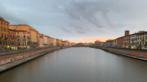 Arch bridge over river amidst buildings in city against sky