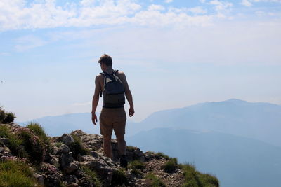 Rear view of male hiker standing on mountain against sky