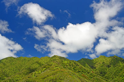 View of mountain ridge line against blue sky with clouds 